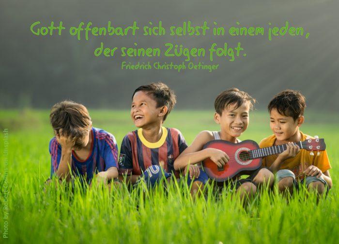 4 lachende Kinder im Gras mit kleiner Gitarre